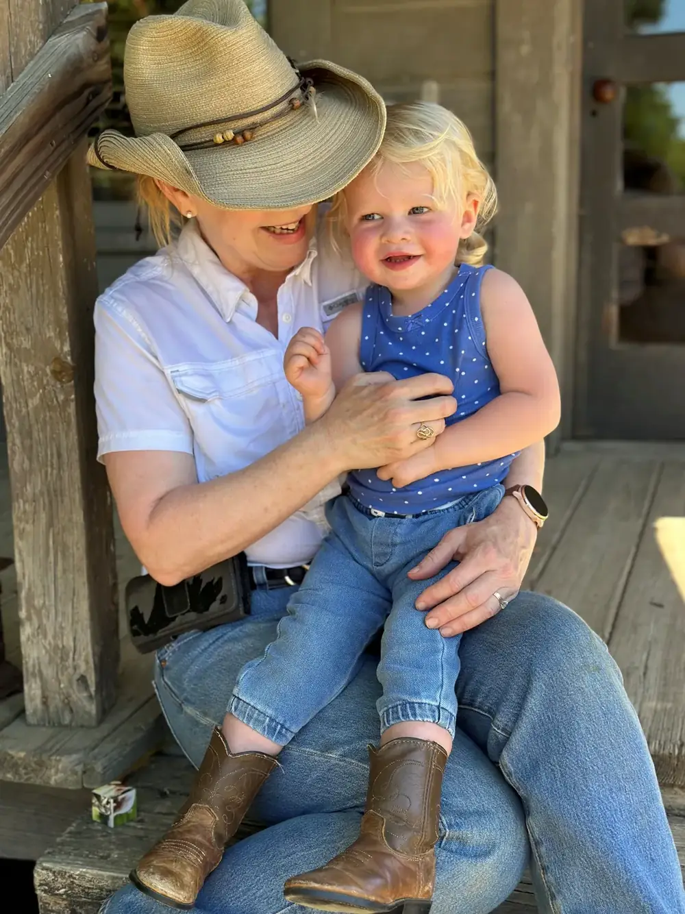 A grandmother in a straw hat holding a toddler on the porch