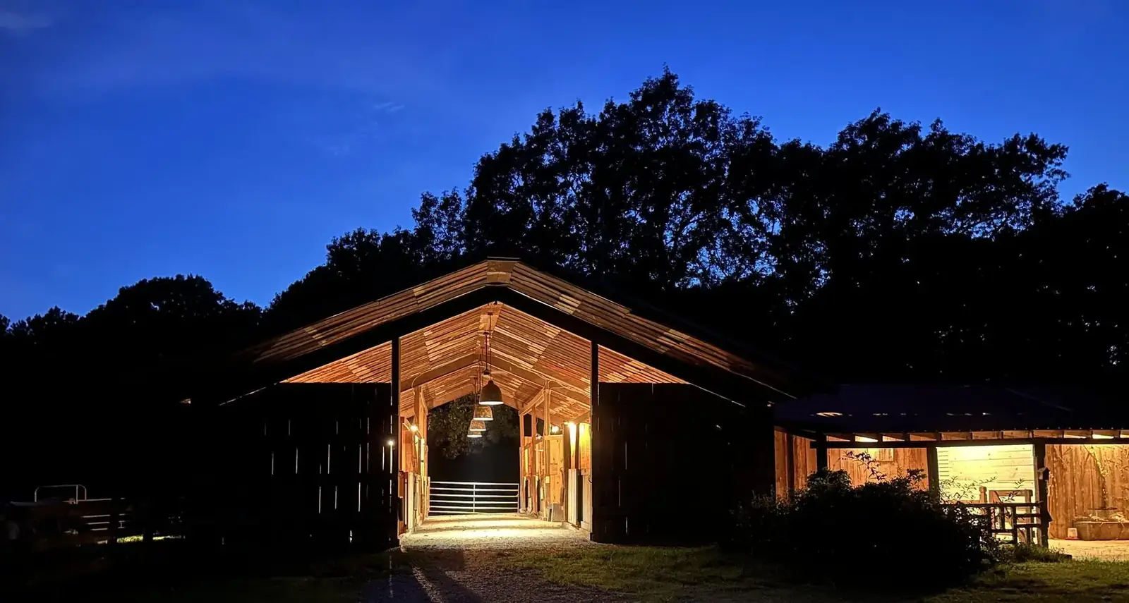 The open cypress barn lit from within at dusk