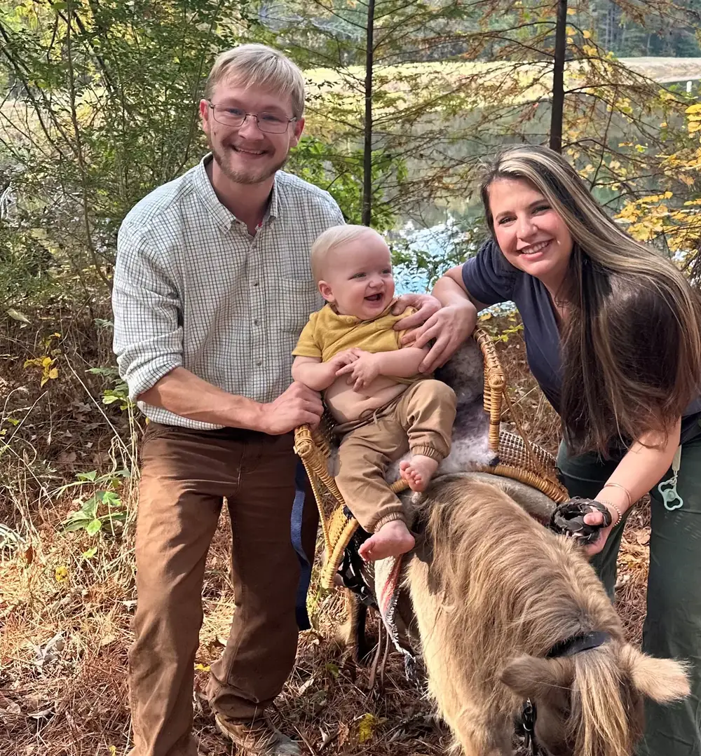 Two adults and a baby beside a miniature horse at the lake